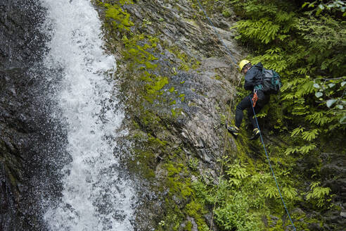 Seitenansicht eines Mannes, der sich neben einem Wasserfall im Canyon abseilt. - CAVF65767