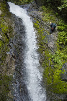 Seitenansicht eines Mannes, der sich neben einem Wasserfall im Canyon abseilt. - CAVF65768