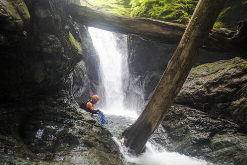Ein Mann wickelt das Seil nach dem Abseilen von einem Wasserfall auf. - CAVF65783
