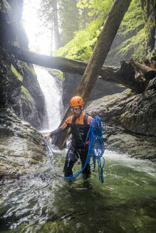 Ein Mann wickelt das Seil nach dem Abseilen von einem Wasserfall auf. - CAVF65784