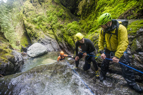 Three adventurous men work as a team to belay friend down waterfall. - CAVF65786