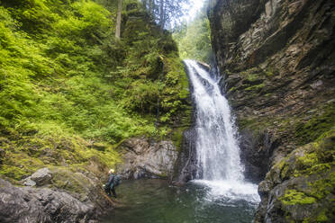 Man steps out of the water after rappelling over a waterfall. - CAVF65798