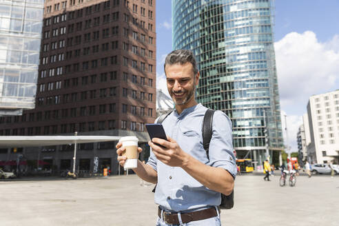 Lächelnder Geschäftsmann mit Blick auf das Smartphone in der Stadt, Berlin, Deutschland - WPEF02066