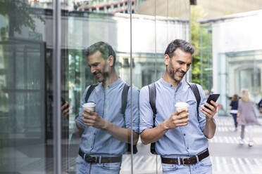 Lächelnder Geschäftsmann mit Blick auf das Smartphone in der Stadt, Berlin, Deutschland - WPEF02069