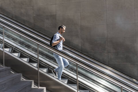 Geschäftsmann geht Rolltreppe in der Stadt hinunter, Berlin, Deutschland, lizenzfreies Stockfoto