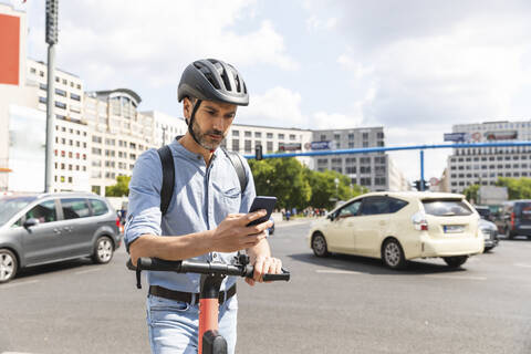 Businessman looking at the smartphone commuting on electric scooter in the city, Berlin, Germany stock photo