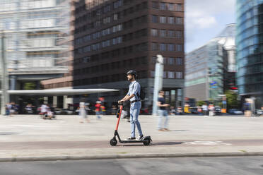 Businessman riding e-scooter on the pavement in the city, Berlin, Germany - WPEF02084