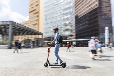 Geschäftsmann fährt E-Scooter auf dem Bürgersteig in der Stadt, Berlin, Deutschland - WPEF02086