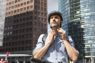 Mann befestigt den Helm vor der Fahrt mit dem Elektroroller, Berlin, Deutschland - WPEF02087