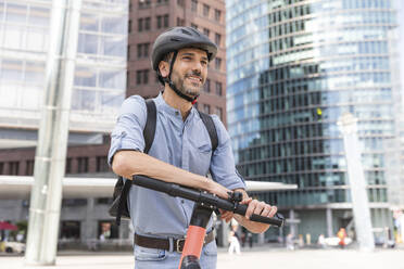 Smiling man with e-scooter on city square, Berlin, Germany - WPEF02090