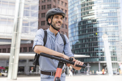 Lächelnder Mann mit E-Scooter auf dem Marktplatz, Berlin, Deutschland - WPEF02090