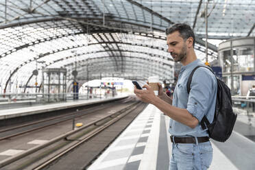 Geschäftsmann am Bahnhof, der auf den Zug wartet und auf sein Smartphone schaut, Berlin, Deutschland - WPEF02094