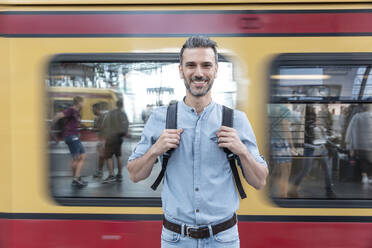 Porträt eines lächelnden Mannes auf dem Bahnsteig mit einem Zug im Hintergrund, Berlin, Deutschland - WPEF02101