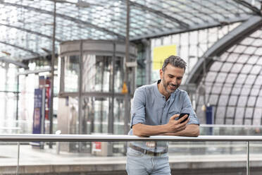 Smiling man at the station looking at the smartphone, Berlin, Germany - WPEF02104