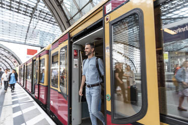Lächelnder Mann beim Aussteigen aus dem Zug auf dem Bahnsteig, Berlin, Deutschland - WPEF02105