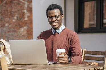 Junger Mann mit Laptop in einem Café, trinkt Kaffee - VPIF01616