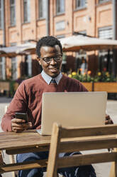 Junger Mann mit Smartphone und Laptop in einem Café - VPIF01622