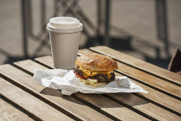 Nahaufnahme eines Cheeseburgers und eines Kaffees zum Mitnehmen auf einem Holztisch - VPIF01626