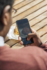 Junger Mann, der seinen Cheeseburger mit seinem Smartphone fotografiert - VPIF01627