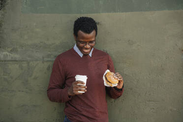 Junger Mann mit einem Cheeseburger und einem Kaffee zum Mitnehmen, Porträt - VPIF01631