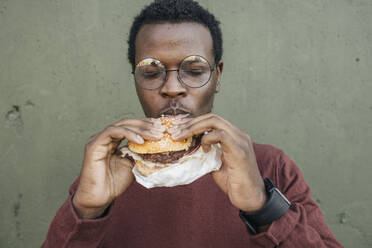 Junger Mann isst Cheeseburger, mit geschlossenen Augen - VPIF01635