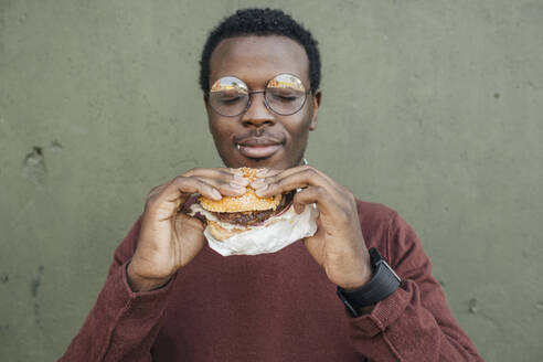 Junger Mann isst Cheeseburger, mit geschlossenen Augen - VPIF01636