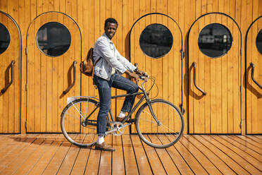 Junger Mann auf dem Fahrrad vor einer Holztür - VPIF01687