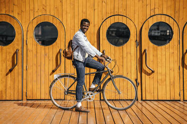 Junger Mann auf dem Fahrrad vor einer Holztür - VPIF01688