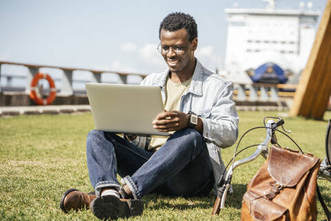 Junger Mann sitzt im Gras und benutzt einen Laptop, lizenzfreies Stockfoto