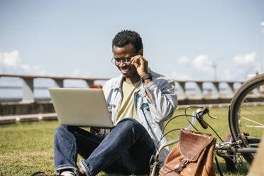 Young man sitting on grass, using laptop - VPIF01697