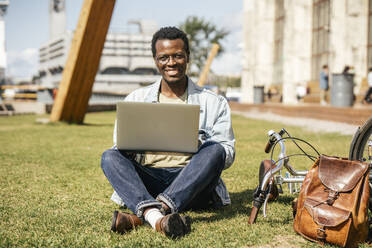 Young man sitting on grass, using laptop - VPIF01698