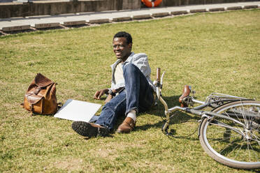 Young man with alptop and bicycle, lying on grass - VPIF01699