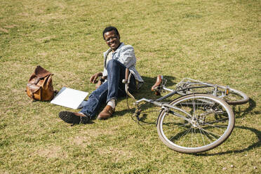 Young man with alptop and bicycle, lying on grass - VPIF01700