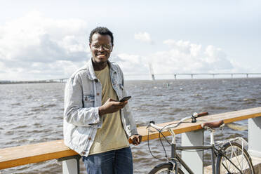 Younh´g man leaning on railing by the sea, using smartphone - VPIF01706