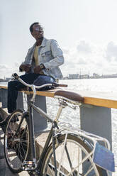 Young amn with bicycle sitting on railing by the sea - VPIF01708