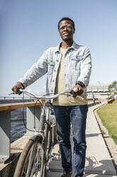 Young man pushing bicycle by the sea - VPIF01715