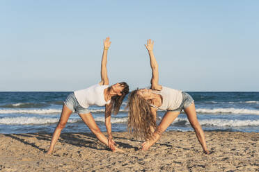 Zwei Frauen praktizieren Acro Yoga am Strand, Dreieckspose - DLTSF00262