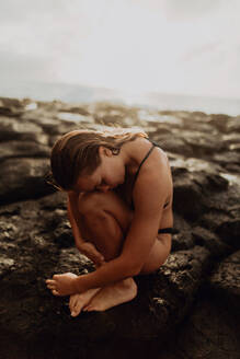 Frau sitzt zusammengerollt auf Felsen am Meer, Princeville, Hawaii, USA - ISF22512