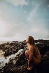 Naked woman sitting on rocks by sea, Princeville, Hawaii, US - ISF22523