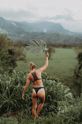 Frau im Bikini hält großes Blatt, Princeville, Hawaii, USA - ISF22532