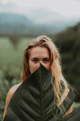 Woman in bikini holding large leaf, Princeville, Hawaii, US - ISF22533