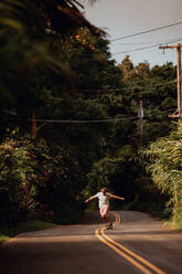 Mittlerer Erwachsener, männlicher Skateboarder, der auf der Mittellinie einer Landstraße Skateboard fährt, Haiku, Hawaii, USA - ISF22595
