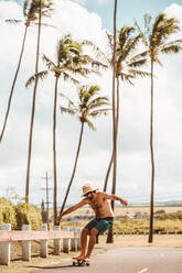 Mittlerer Erwachsener, männlicher Skateboardfahrer mit Strohhut, Skateboarding auf der Küstenstraße, Haiku, Hawaii, USA - ISF22693