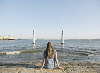Rear view of woman sitting at the coast, Lisbon, Portugal - AHSF00998