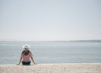 Rückansicht einer Frau, die an der Küste sitzt, Lissabon, Portugal - AHSF01001