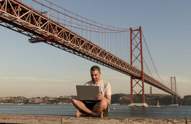 Mann mit Laptop an der Brücke des 25. April in Lissabon, Portugal - AHSF01013