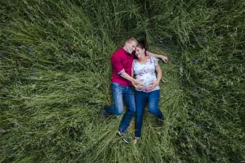 Schwangere Frau und Mann mit Babybauch, auf der Wiese liegend, lizenzfreies Stockfoto