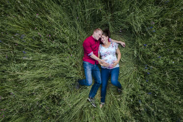 Schwangere Frau und Mann mit Babybauch, auf der Wiese liegend - HMEF00661