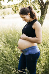 Junge schwangere Frau mit Babybauch, stehend auf einer Wiese - HMEF00663