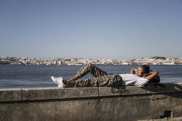 Junge Frau liegt auf einer Mauer am Wasser, Lissabon, Portugal - UUF19069